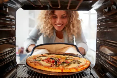 Uśmiechnięta kobieta wyjmuje z piekarnika pyszną pizzę. Idealna temperatura do pieczenia pizzy to klucz do sukcesu.