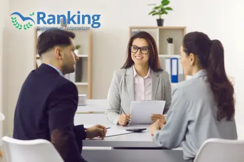 Trzy osoby przy stole w biurze, doradca finansowy z dokumentami rozmawia z parą.