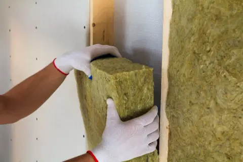 Manos con guantes instalan aislamiento en paredes. El aislamiento térmico de paredes tiene un precio competitivo.