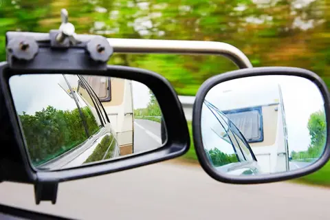 Zwei Spiegel zeigen die Straße und einen Wohnwagen. Für sicheres Fahren mit Anhänger ist der Wohnwagenspiegel Pflicht.