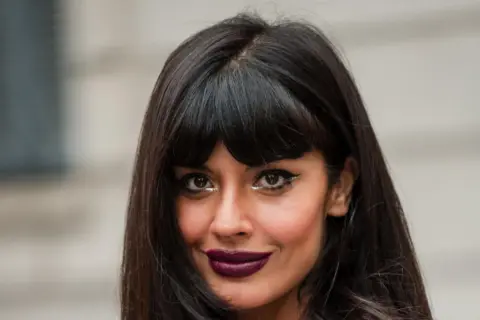Frau mit dunklem Haar und Pony, der gerade rauswächst, und auffälligem Make-up.