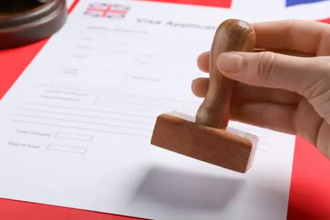 Dłoń trzyma pieczątkę nad formularzem wniosku o wizę do Anglii.