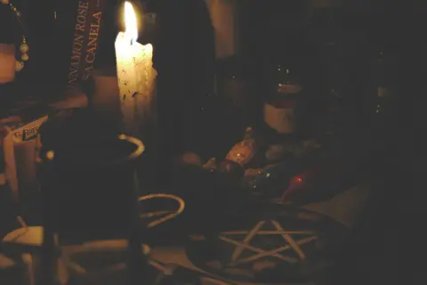 Mroczna atmosfera, płonąca świeca, książka z napisem "Cinnamon Rose", muszelki i pentagram. Czy pentagram jest zły? To zależy od intencji.