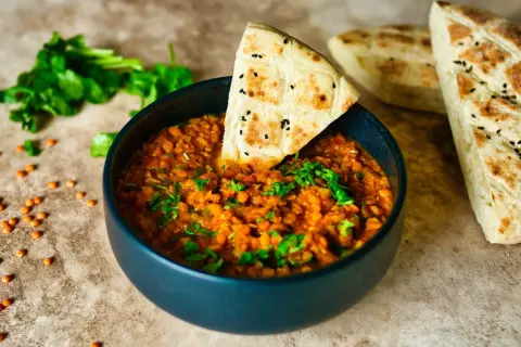 Herzhaftes Linsengericht in einer Schüssel, garniert mit frischer Petersilie und einem Stück Fladenbrot. Perfekt für Linsen Rezepte.