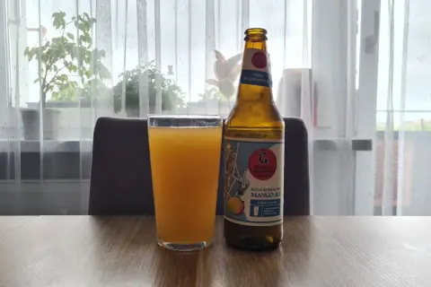Szklanka z pomarańczowym napojem i butelka piwa bezalkoholowego mango ale na stole.