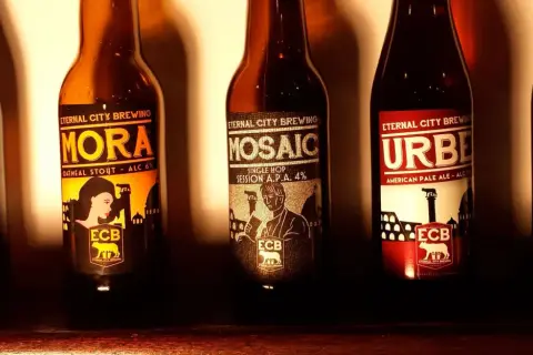Cinque bottiglie di birra artigianale di Eternal City Brewing, con etichette raffiguranti monumenti e figure iconiche.