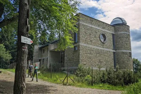 Kamienny budynek obserwatorium astronomicznego na szczycie góry. Obok tabliczka szlaku turystycznego PTTK.