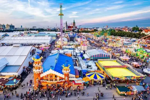Aerial view of a crowded Oktoberfest fairground with tents, rides, and people.