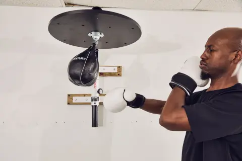 A man in boxing gloves trains with a speed bag, working his shoulder and arm muscles.