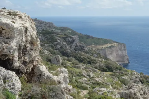 Malta's dramatic Dingli Cliffs, a rugged coastline meeting the deep blue sea under a cloudy sky.