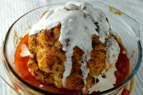Hel blomkål i ugn, gyllene och kryddad, badar i en smakrik tomatsås och toppas med en krämig sås. En festlig rätt!