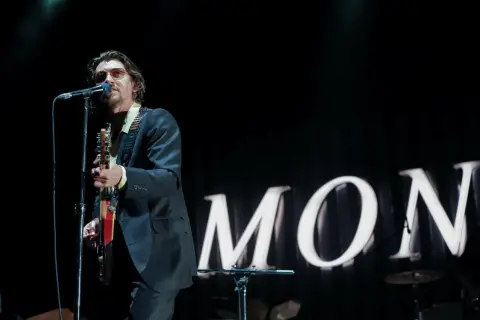 Alex Turner w okularach przeciwsłonecznych śpiewa i gra na gitarze podczas jednego z koncertów Arctic Monkeys.
