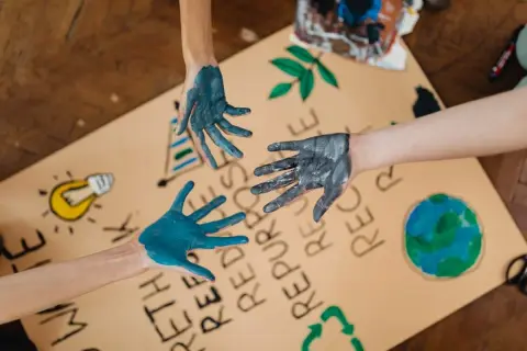 Manos pintadas de azul y gris sobre un cartel con dibujos de la Tierra, una bombilla y el símbolo de reciclaje. Un llamado a la acción para salvar el planeta.