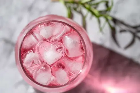 En rosa drink med hjärtformade isbitar och en rosmarinkvist.