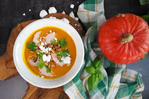 Pomarańczowa zupa dyniowa z mięsem, serem feta, orzeszkami i kolendrą, obok dynia.