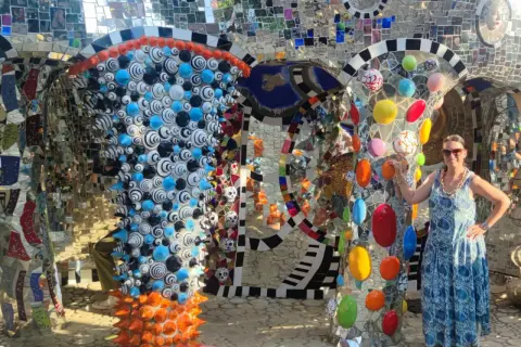 Donna sorride nel Giardino dei Tarocchi, un luogo magico pieno di mosaici colorati e sculture bizzarre.