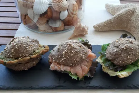 Tre panini low carb ricetta: uno con pesto, uno con salmone affumicato e insalata, uno con formaggio e insalata. Decorazioni marine sullo sfondo.