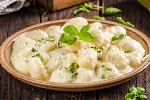 Pyszne gnocchi z kurczakiem w kremowym sosie, posypane parmezanem i świeżą bazylią. Idealne danie na obiad.