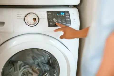 Ręka naciska przyciski na pralce Samsung, pokazując, jak zresetować pralkę Samsung.