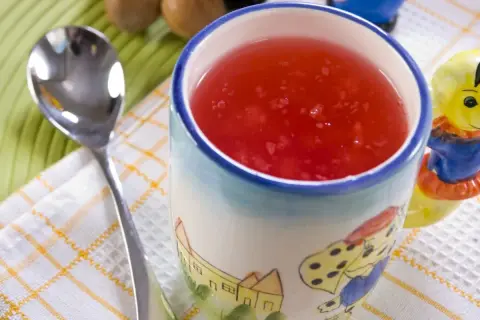 Czerwony kisiel w kubeczku z bajkowym wzorem, obok łyżeczka. Idealny deser, gdy liczymy kisiel kcal.