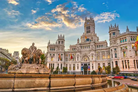 Cibelesfontänen framför det ståtliga Palacio de Comunicaciones, ett ikoniskt konstmuseum i Madrid, under en dramatisk solnedgång.