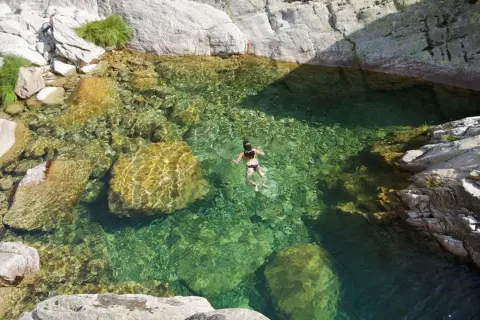 Una persona nada en pozas naturales de agua cristalina en la sierra de Madrid, rodeada de rocas y vegetación.