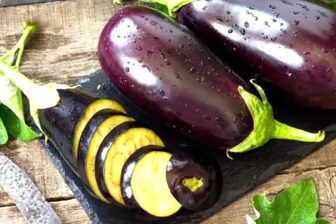Berenjenas frescas, una cortada en rodajas, mostrando su interior amarillo. ¡Se puede comer la berenjena cruda!
