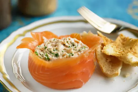 Ein appetitlicher **Salat mit Fisch**, serviert in einem Lachs-Cup, mit knusprigen Brotscheiben und einer goldenen Gabel.