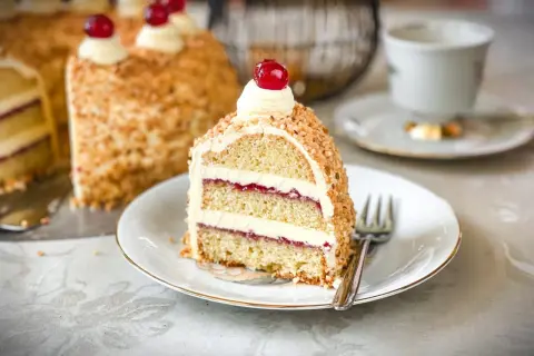 Ein Stück Frankfurter Kranz mit Buttercreme und Kirschen, umhüllt von gehackten Nüssen. Ein Genuss für jeden Kaffeetisch.