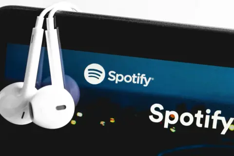 Białe słuchawki wiszą na ekranie smartfona z logo Spotify.