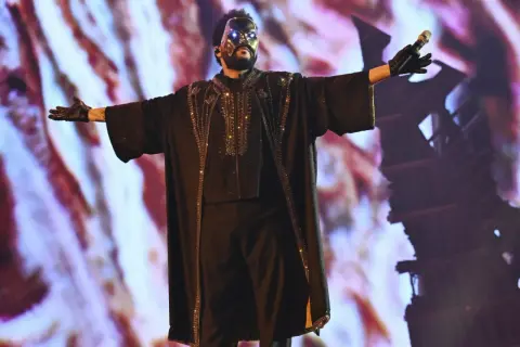The Weeknd w masce i błyszczącym stroju na koncercie w Polsce, z rękami rozłożonymi szeroko.