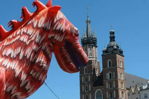 Smok wawelski, znany z atlas obscura krakow, wita turystów na tle Kościoła Mariackiego.