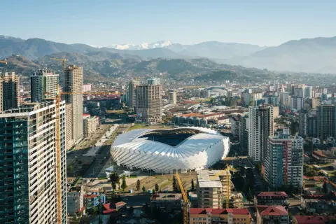 Widok na nowoczesne miasto z futurystycznym stadionem i górami w tle. Rozwój infrastruktury, budowa nowych wieżowców. Batumi ceny nieruchomości mogą być tu atrakcyjne.