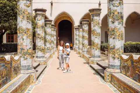 Cortile con colonne decorate a maiolica, un classico del museo Napoli. Una madre e un figlio passeggiano tra gli archi.