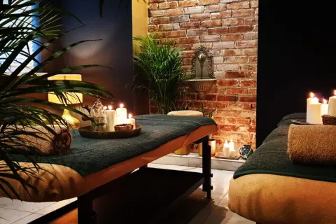 Dwie łóżka do masażu w przytulnym spa, ozdobione świecami i roślinnością.
