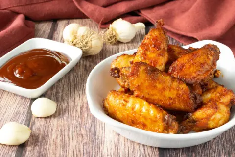 Alette di pollo croccanti e dorate, appena sfornate dalla friggitrice ad aria, servite con salsa barbecue e aglio.