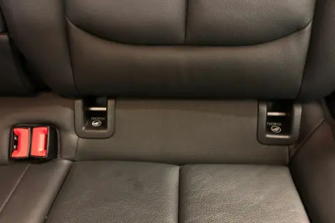 Widok na tylne siedzenia samochodu z widocznymi zaczepami **isofix jak wygląda** oraz czerwonymi klamrami pasów bezpieczeństwa.