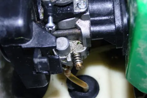 Zbliżenie na gaźnik do kosy spalinowej, widoczne elementy metalowe i plastikowe, przewód paliwowy.