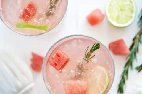 Två glas med en rosa, alkoholfri drink med is, vattenmelonbitar, lime och rosmarin. Perfekt för en sommardag.