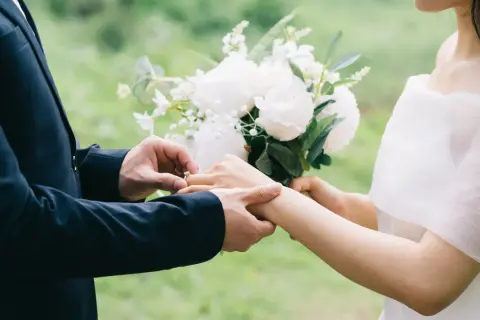 Un homme en costume met une bague à la main d'une femme, bouquet de fleurs blanches. Un poème mariage Baudelaire pour un amour éternel.