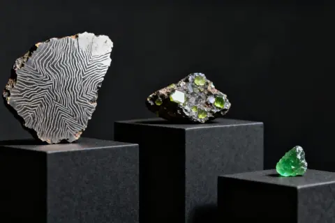 Fragmento de roca con patrón de líneas blancas sobre fondo negro, junto a cristales verdes. Explorando el cristal de roca propiedades.