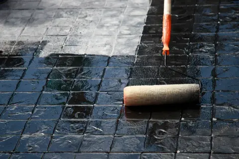 Eine Rolle versiegelt Terrassenplatten, die von dunkel glänzend zu matt wechseln.