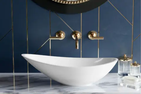 Elegancka, biała umywalka na nodze w łazience z granatową ścianą i złotymi detalami.