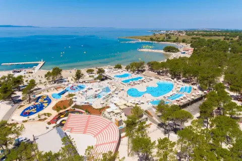 Widok z lotu ptaka na kompleks basenów i plażę z turystami w słoneczny dzień.