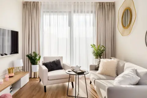 Przytulny salon w stylu minimalistycznym. Jasna kanapa, fotel, stolik kawowy i telewizor tworzą harmonijną przestrzeń.