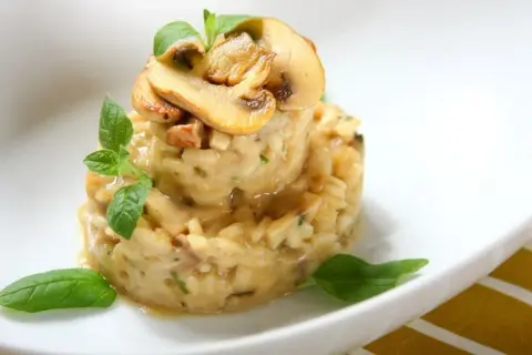 Aromatyczne risotto szafranowe z grzybami, udekorowane świeżą bazylią.