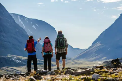 Två vandrare med ryggsäckar blickar ut över en dalgång i Abisko. En pekar mot bergen.