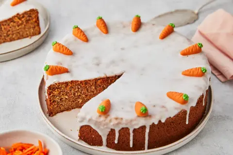Ein saftiger karottenkuchen ohne mehl, verziert mit kleinen Marzipan-Karotten und Zuckerguss. Ein Stück ist bereits angeschnitten.