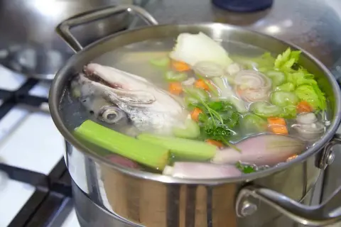 Une tête de poisson nage dans un bouillon avec des légumes, promettant un fumet de poisson savoureux.