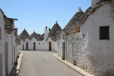 Strada tra i trulli, un incantevole esempio dei borghi da visitare in Puglia. Case bianche con tetti conici in pietra sotto un cielo azzurro.